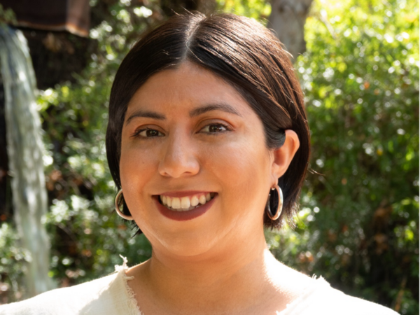 Female with short, brown hair faces the camera smiling in front of a tree.